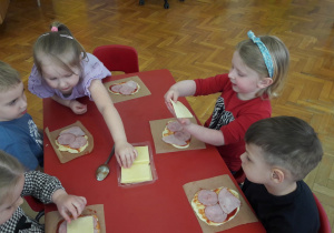 dzieci układają plastry żółtego sera na swoich pizzach
