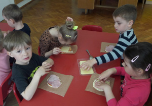 dzieci układają plastry żółtego sera na swoich pizzach