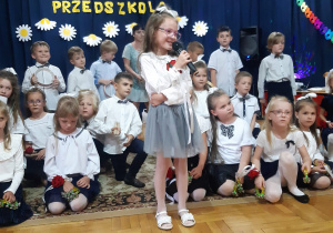 dzieci z grupy III na uroczystości pożegnania przedszkola - dziewczynka recytuje wiersz na tle innych dzieci ze swojej grupy