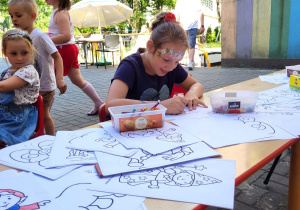 dziewczynka maluje kolorowanki rozłożone na stolikach na tarasie przedszkolnym