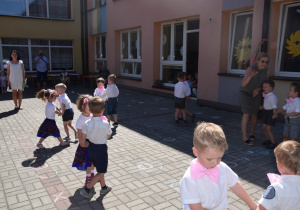 dzieci z grupy I tańczą w parach na tarasie przedszkolnym trzymając się za ręce, ubrane w białe koszulki z różowymi muchami