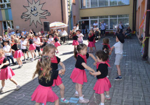 "Polka cowboyka" taniec dzieci z grupy VIII w parach - dziewczynki w różowych spódniczkach i chustkach oraz w czarnych podkoszulkach a chłopcy w krótkicj spodenkach, białych koszulach i kapeluszach na tarasie przedszkolnym tańczą w parach po kole