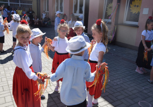 dzieci z grupy III tańczą w kołach - dziewczynki są w białych bluzkach i hiszpańskich spódnicach oraz z czerwonym kwiatem we włosach, natomiast chłopcy w białych kapeluszach i koszulach i ciemnych spodniach