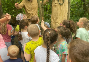 dzieci stoją przed skrzatem i rzeżbą z pnia drzewa w kształcie siedzącego skrzata i głową niedźwiedzia