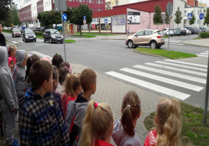 dzieci stoją przy drodze z pasami i obserwują ruch uliczny na skrzyżowaniu
