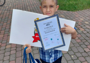 chłopiec z dyplomem i nagrodami otrzymanymi w konkursie