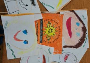 flagi wykonane przez dzieci z logo przedszkola - słoneczkiem a po drugiej stronie z autoportretami dzieci