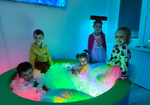 dzieci w sali doświadczania świata - doświadczają światła i kolorów w basenie z przezroczystymi kulkami