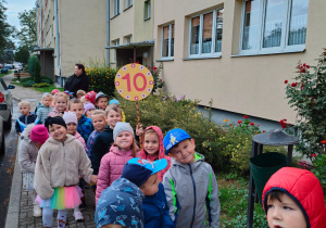przedszkolaki maszerują ulicami osiedla z emblematem z "10"