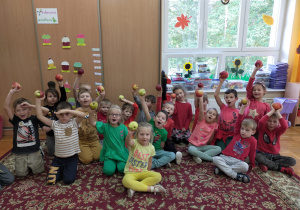 dzieci z grupy III trzymają jabłka w ręce uniesionej do góry