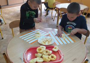 dzieci przy stolikach kroją obrane jabłka na plastry do suszenia