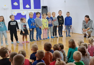 dzieci śpiewają piosenkę a obok kuca nauczycielka