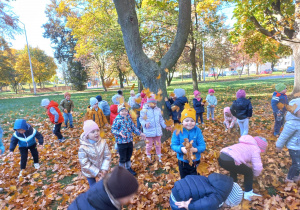 przedszkolaki w parku rzucają do góry kolorowymi liśćmi