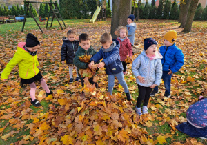 dzieci w ogrodzie przedszkolnym gromadzą kolorowe liście na domek dla jeża