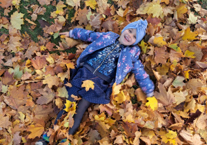 dziewczynka leży na kolorowych liściach i robi "aniołka"