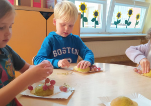 dzieci robią owocowe jeżyki z połowy zielonej gruszki i różowego winogrona nakłuwanego na wykałaczki