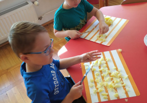 przy stoliku, na tackach chłopcy kroją ziemniaki na drobne kawałki do sałatki warzywnej