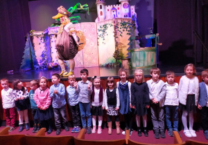 w teatrze - przedszkolaki stoją przed sceną a na niej aktor przebrany za Złotą Kaczkę