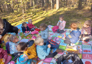maluszki siedzą na matach w lesie i piknikują