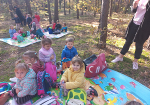 dzieci siedzą na kolorowych matach w lesie