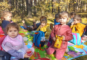 przedszkolaki jedzą swoje słodkości siedząc na polanie w lesie na kolorowych matach