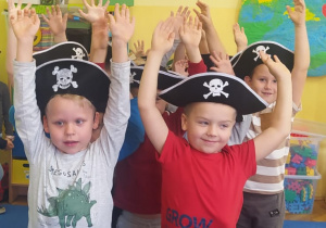chłopcy w czapkach piratów stoją w grupie z rękami uniesionymi wgórę