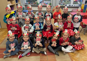 dzieci z grupy VII pozują do zdjęcia grupowego w czerwonych opaskach z naklejonym obrazkiem Myszki Miki i portretem Myszki Miki w dłoniach (kolorowanka)
