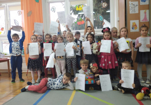 dzieci z grupy IV pozują do zdjęcia grupowego trzymając w dłoniach kartkę z napisem "Dzień Myszki Miki"