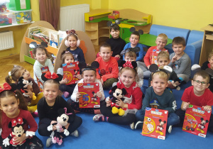 dzieci z grupy VIII pozują do zdjęcia grupowego w czarnych opaskach z uszami Myszki Miki i książeczkami oraz maskotkami Miszki Miki