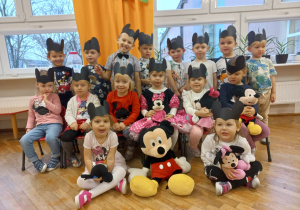 dzieci z grupy VIII pozują do zdjęcia grupowego w czarnych opaskach z uszami Myszki Miki i maskotkami Miszki Miki