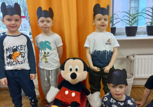 czterech chłopców stoi wokół dużej maskotki Myszki Miki siedzącej na krzesełku