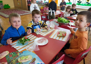 dzieci siedzą przy stolikach i komponują własne kanapki z warzyw, wędliny i żółtego sera