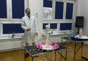 chemik demonstruje białą lawę wulkaniczną, która wystrzela z butelki i opadając w dół rozpryskuje się na tacy
