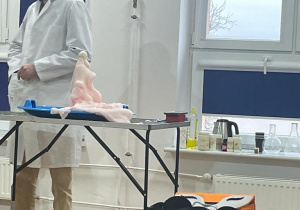 chemik stoi przy stole, na którym widać lawę wulkaniczną w kolorze lekko różowym wypływającą z butelki na tacę