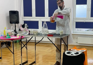 chemik przelewa płyn w kolorze herbaty do pojemnika, w którym zmienia swój kolor na herbaciany