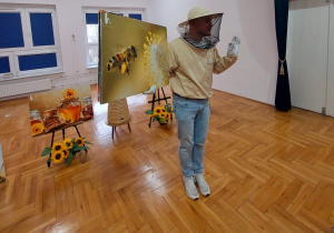 pszczelarz w kapeluszu z siatką trzyma ilustrację pszczoły i pokazuje dzieciom