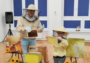 pszczelarz i chłopiec w kapeluszach z siatką trzymają kratki z woskiem umieszczane w ulu