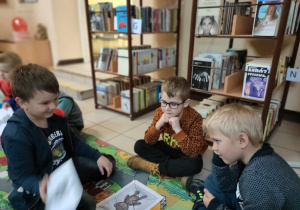 w bibliotece - chłopcy siedzą wokół ułożonych puzzli z misiem