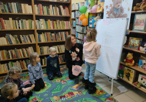 w bibliotece - dzieci siedzą i obserwują jak koleżanka rysuje misia na dużym, białym arkuszu papieru