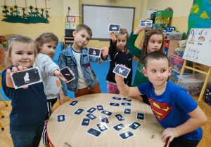przedszkolaki stoją wokół stołu i losują karty z obrazkami przyszłych zawodów dzieci