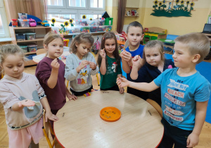 dzieci stoją wokół stolika i trzymaja i wrzucają monety do talerzyka z wodą