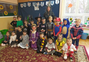 zdjęcie grupowe dzieci z nauczycielką w różnych bajkowych kostiumach na tle napisu "Andrzejki"