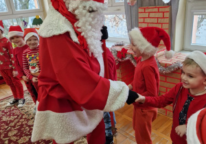 Mikołaj podaje dzieciom rękę witając się z każdym dzieckiem stojącym w kole