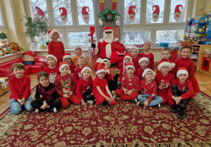 dzieci z grupy III w czerwonym ubraniach pozują do zdjęcia z Mikołajem