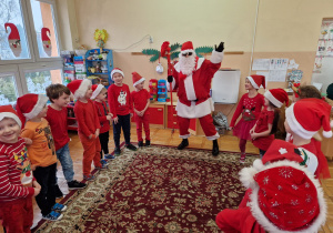 Mikołaj stoi z dziećmi w kole i macha ręką