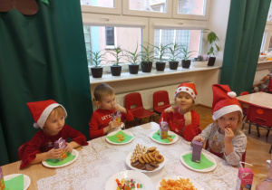 przedszkolaki w czerwonych ubraniach siedzą przy stolikach i częstują się słodkościami
