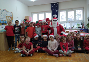 dzieci z grupy IV w czerwonym ubraniach pozują do zdjęcia z Mikołajem