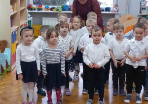 dzieci z grupy VII stoją w grupie w białych bluzkachi ciemnych spódnicach i spodniach