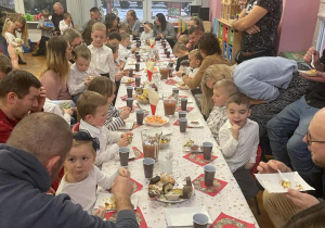 przedszkolaki z bliskimi siedzą przy świątecznie udekorowanych stołach i częstują się słodkościami