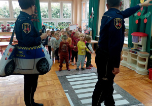 funkcjonariusze straży miejskiej uczą dzieci jak należy rozglądać się przed przejściem po pasach
